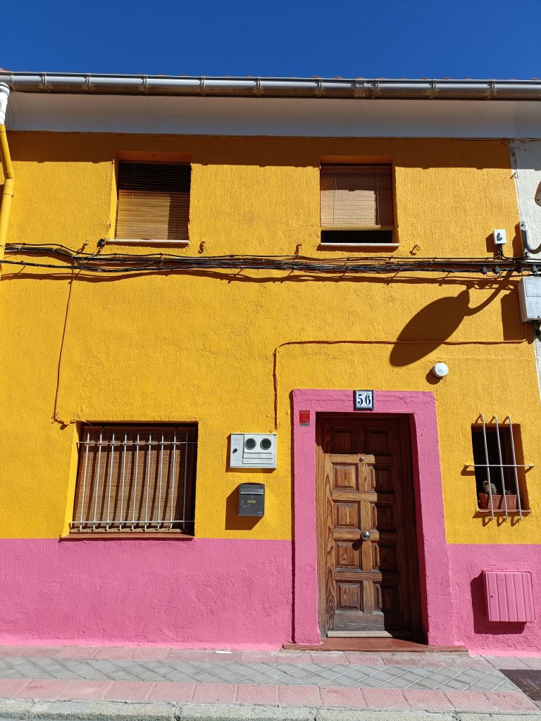 Dwukolorowy budynek, dół budynku na ¼ wysokości jest w kolorze różowym, reszta w kolorze żółtym. Drewniane drzwi obwiedzione są framuga w kolorze różowym. W oknach na parterze piętrze znajdują się kraty, okna na pierwszym piętrze mają słomiane żaluzje. Nad budynkiem jasne niebieskie niebo.